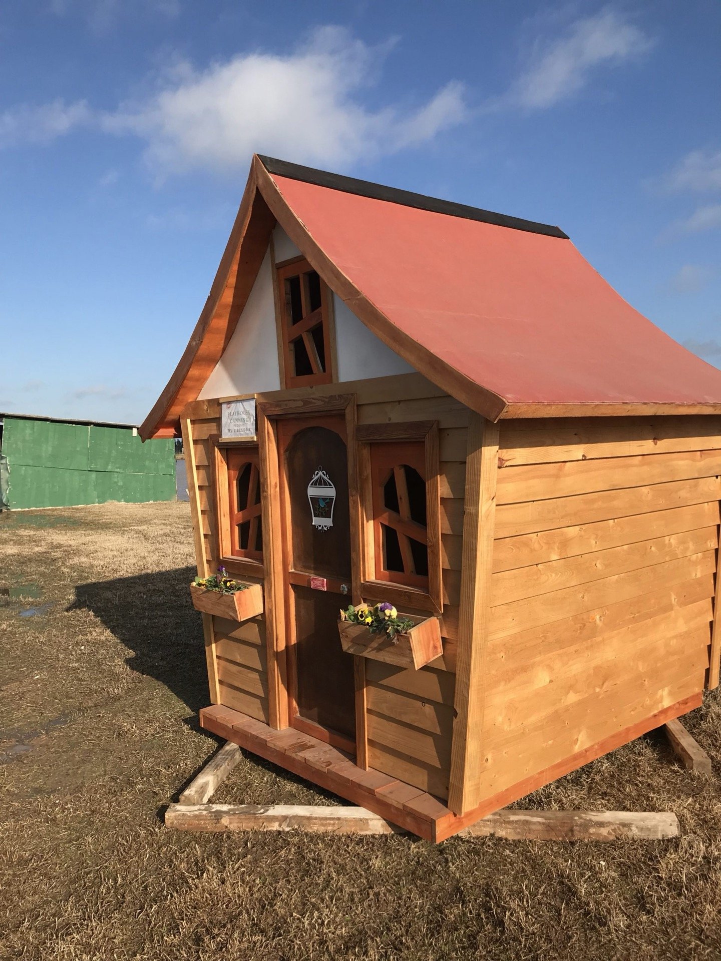 Casita de madera con techo rojo y jardinera, vista tres cuartos
