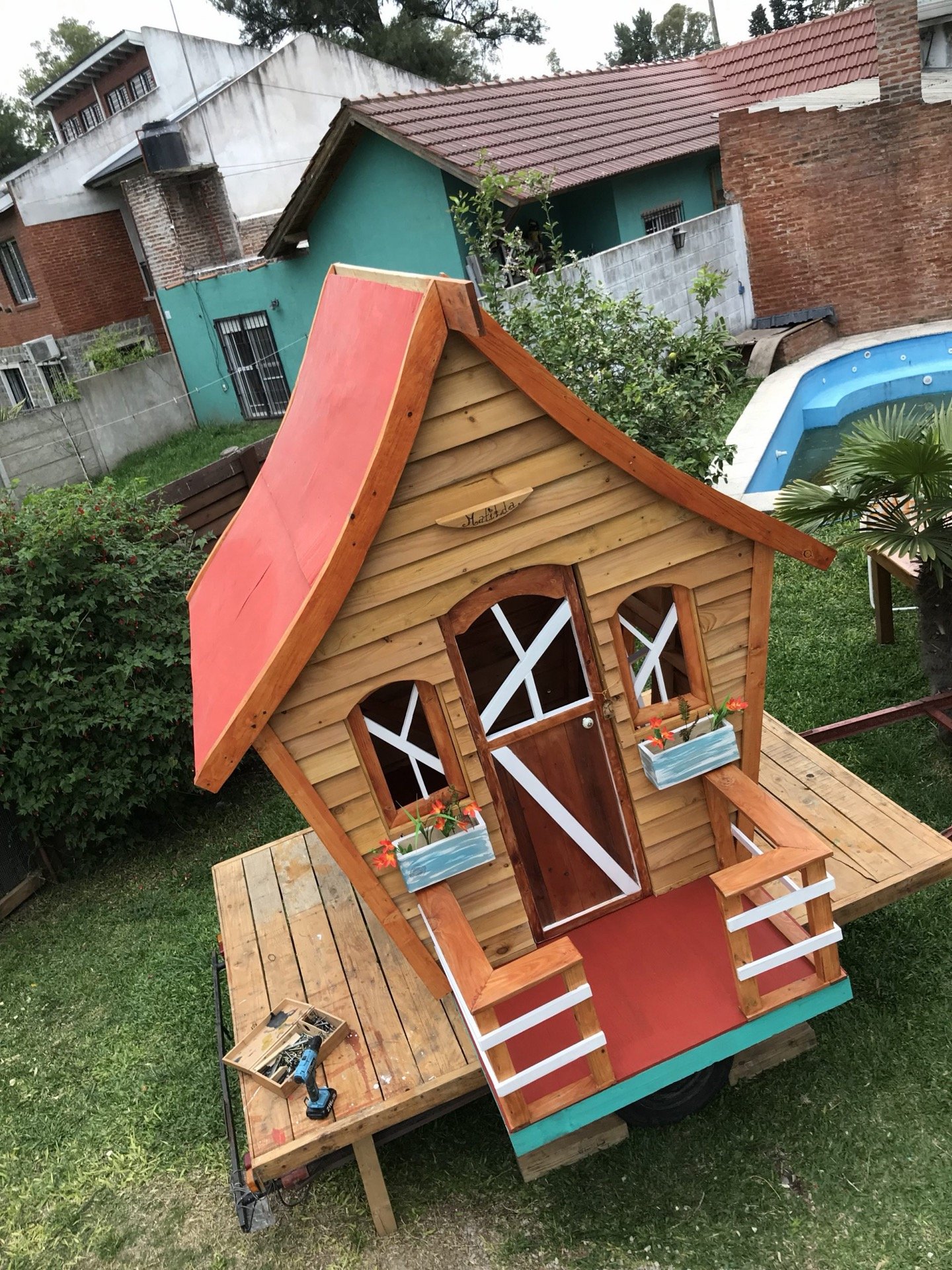 Casita torcida de cuento con techo rojo, macetas y puertas cruzadas